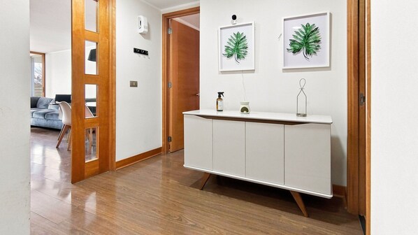 A hallway with a wooden door, a white cabinet with a mirror, and framed leaves on the wall.