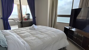 Habitación de hotel con una cama grande, un televisor sobre un soporte de madera y vistas al mar a través de la ventana.