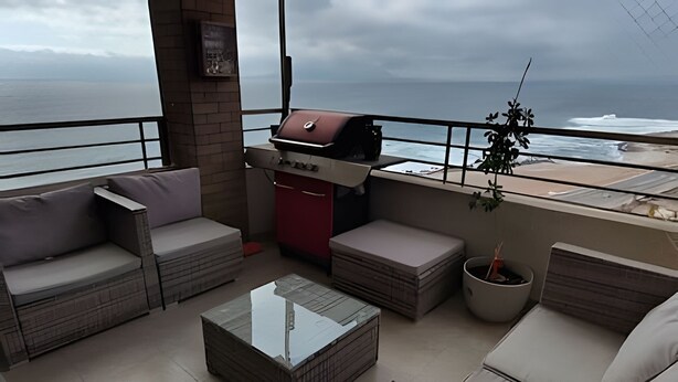 Un balcón con parrilla, zona de estar y vista al océano.