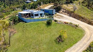 A modern, two-story house with a covered patio and a dirt road leading to it. - Ocean View Escape - less than 5 min to the highway (Sandy Beach)