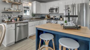 Una cocina moderna con armarios blancos, electrodomésticos de acero inoxidable y una isla de madera con taburetes.