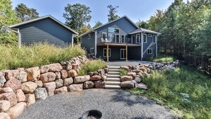 A two-story house with a stone retaining wall and a gravel driveway. - New Modern Construction on McNutt Lake, Minutes from downtown Minocqua! (Minocqua)