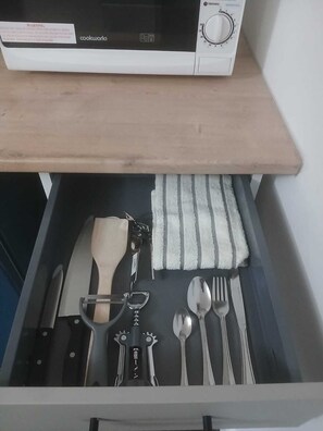 Un cajón con un cuchillo, una espátula, un abrelatas, una cuchara, un tenedor y una servilleta.
