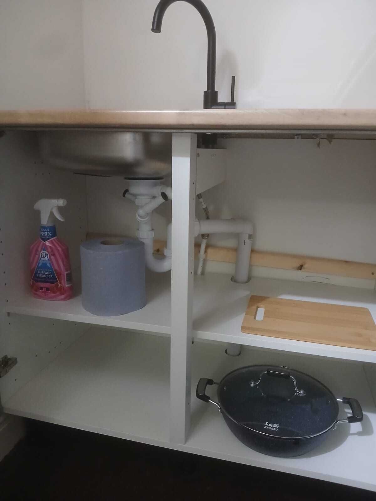 A kitchen with a sink, a roll of paper towels, a spray bottle, and a pan on the countertop.