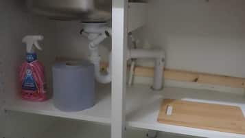 A kitchen with a sink, a roll of paper towels, a spray bottle, and a pan on the countertop.