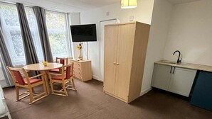 A room with a dining table, chairs, a TV, a wardrobe, and a kitchenette. - Ground-Floor Family Studio Apartment with Double and Single Beds – Free Parking (Gosport)