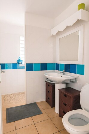 A bathroom with a white sink, a mirror, a toilet, and a small cabinet.