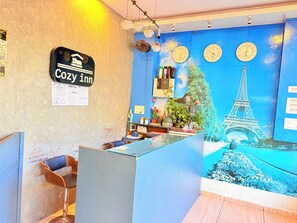 A reception desk with a clock, a sign reading 'Cozy Inn,' and a wall mural of the Eiffel Tower. - Cozy Inn T2 Mumbai Airport (Mumbai)