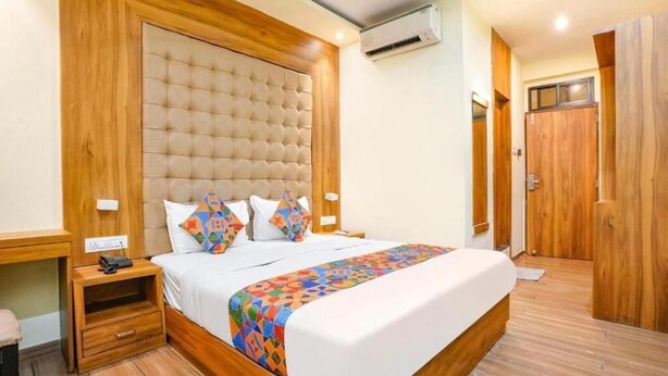 A bedroom with a large bed, wooden headboard, bedside tables, and a wooden floor. - Cozy Inn T2 Mumbai Airport (Mumbai)