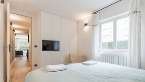 Ein modernes Hotelzimmer mit einem großen Bett, einem an der Wand montierten Flachbildfernseher und Blick ins Freie durch ein Fenster.