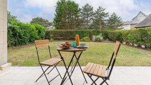 Eine Terrasse im Freien mit zwei Holzstühlen, einem Tisch, einem Esskorb und einer Flasche.