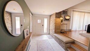A modern entryway with a wooden bench, a round mirror, and a stone accent wall. - Luxury 4-bedroom house with AC/Heat in Buffalo (Buffalo)
