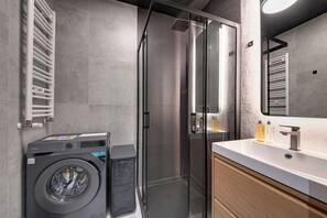 A modern bathroom with a glass shower enclosure, a built-in washing machine, and a vanity with a mirror. - RentPlanet - Studio Hallera (Wrocław)