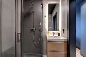 A modern bathroom with a glass-enclosed shower, a wooden vanity with a mirror, and a blue door.