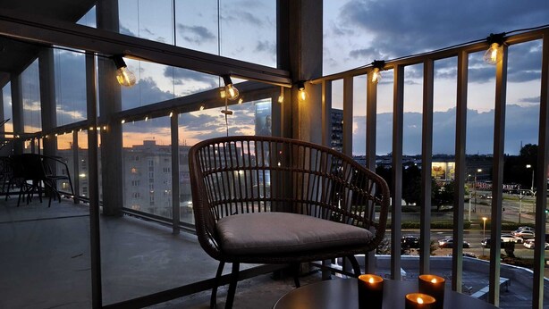 Un balcone con una sedia in vimini, un tavolino con candele e luci a tendina.
