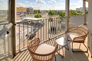 A balcony with wicker chairs and a small table, overlooking a parking lot and buildings. - RentPlanet - Studio Hallera (Wrocław)