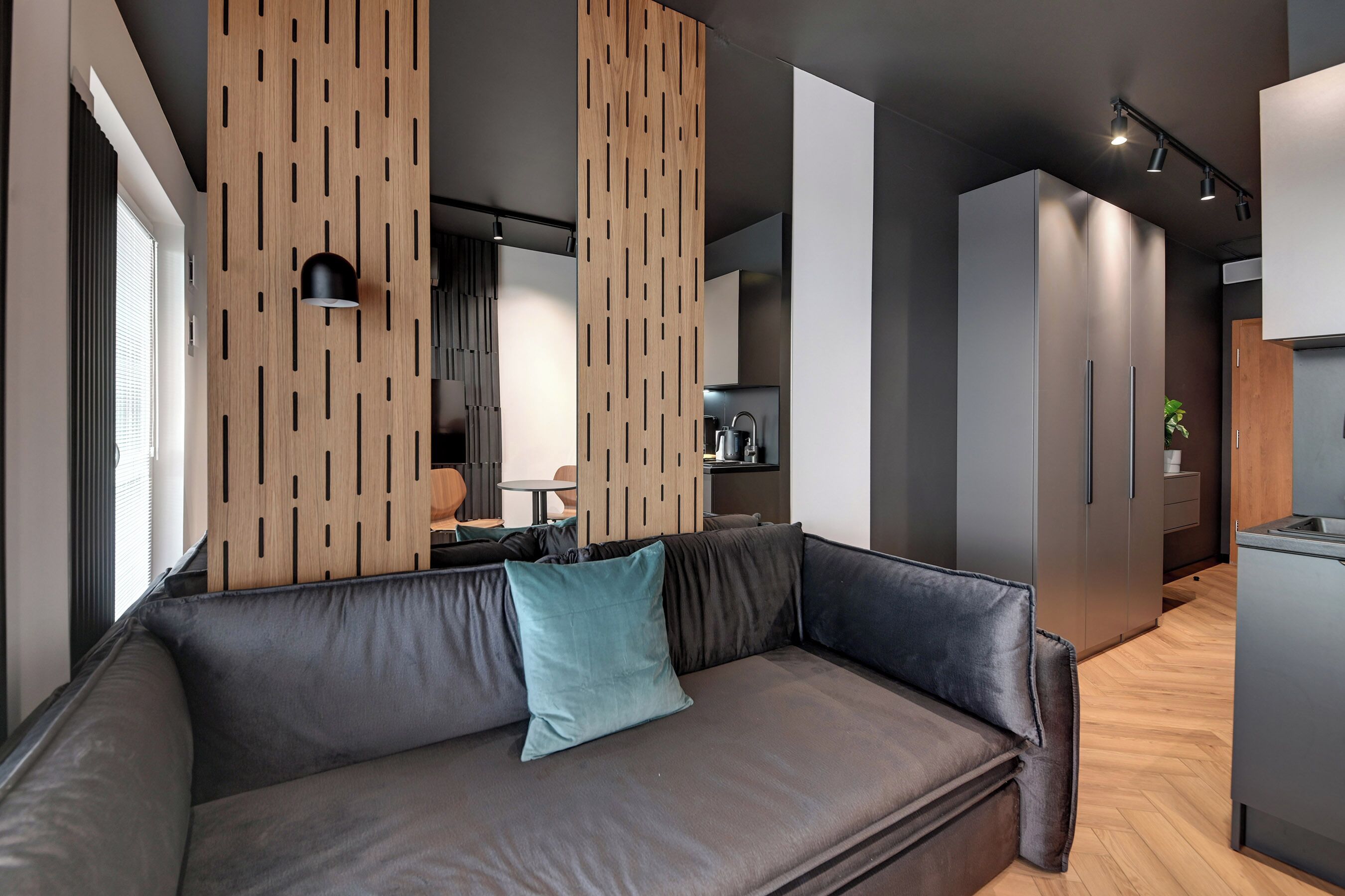 Un área de estar moderna con un sofá, paneles de pared de madera, una cocina al fondo y un comedor.