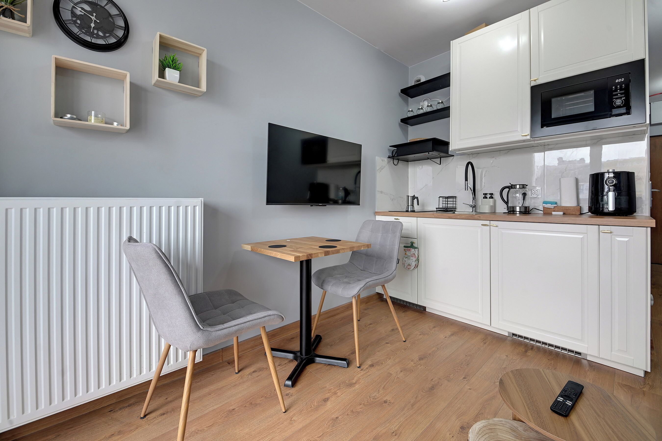 A modern kitchen with white cabinets, a microwave, and a TV mounted on the wall.