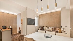 A modern hotel room with a dining area, a sofa, and a TV mounted on the wall.