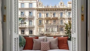 Un balcon agrémenté d’un canapé et de coussins, d’où l’on peut admirer une rangée d’immeubles à l’architecture riche et élaborée.