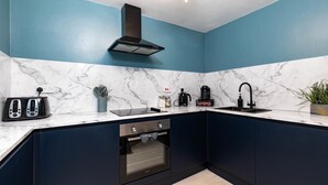 Une cuisine avec un mur bleu, un plan de travail en marbre blanc, une hotte noire, un grille-pain, une machine à café et un four.