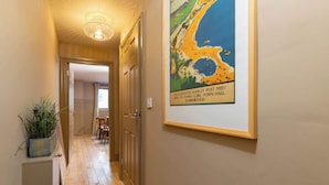 Un couloir au plancher en bois, une carte encadrée accrochée au mur et une porte donnant sur une pièce.