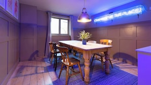 Un espace repas comprenant une table en bois, des chaises, un luminaire suspendu et un néon fixé au mur.