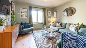 Un salon avec un canapé, une table basse et un meuble en bois. Il y a des affiches au mur et une fenêtre avec des rideaux.