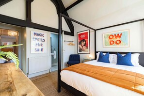 Ein Schlafzimmer mit einem Bett, einem Holztisch und einem Hängesessel. An der Wand befinden sich zwei gerahmte Bilder.