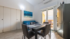 Una cocina compacta con refrigerador, una mesa de comedor con sillas, un sofá y un ventanal corredizo que da a un espacio exterior.