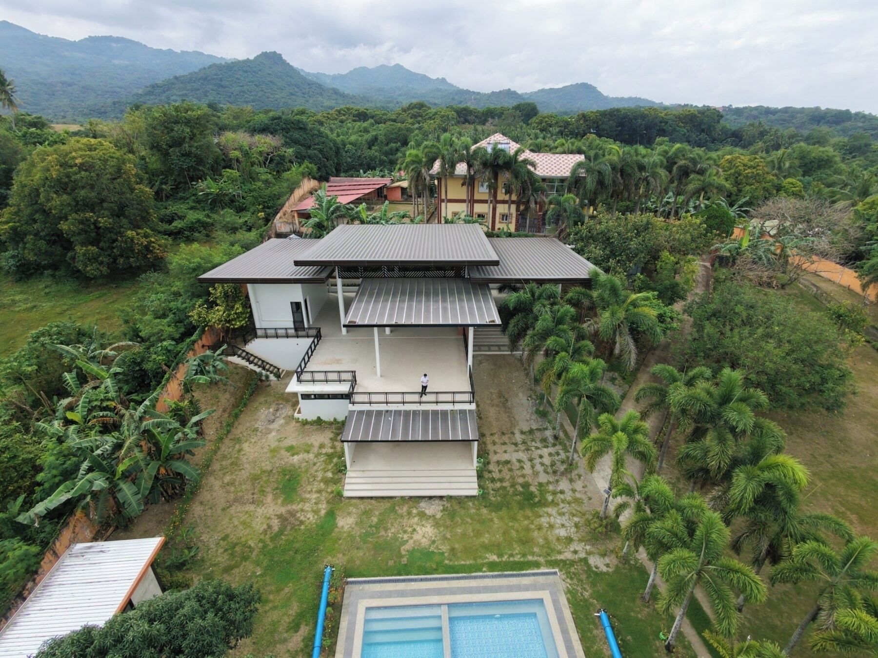 A modern house with a large patio, surrounded by lush greenery and mountains in the background.