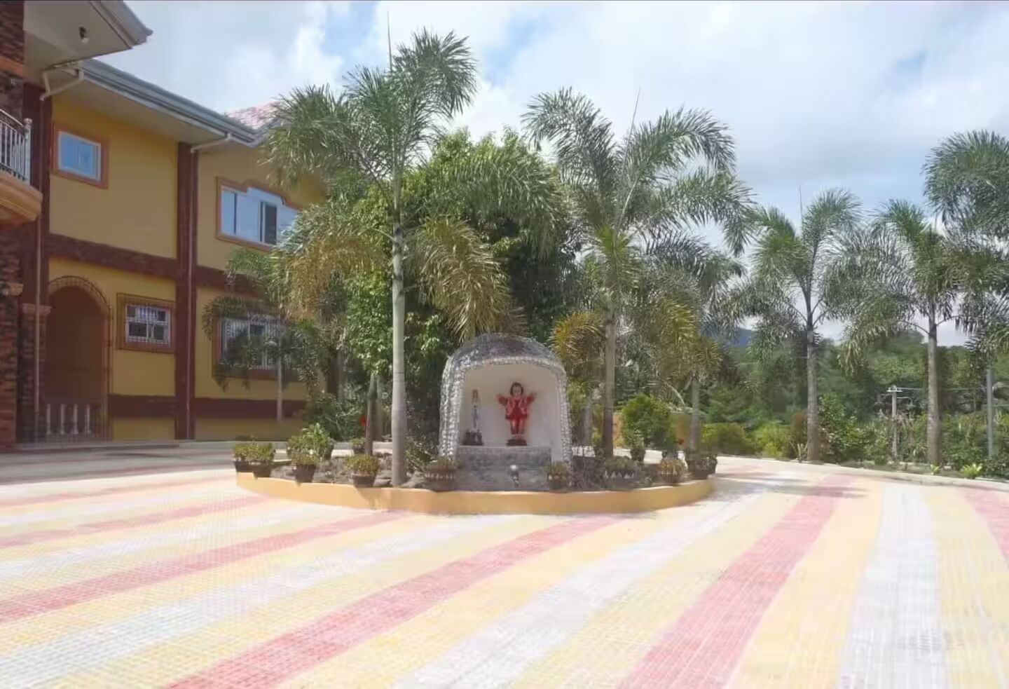 A building with a yellow facade, a central courtyard with a statue, and palm trees.