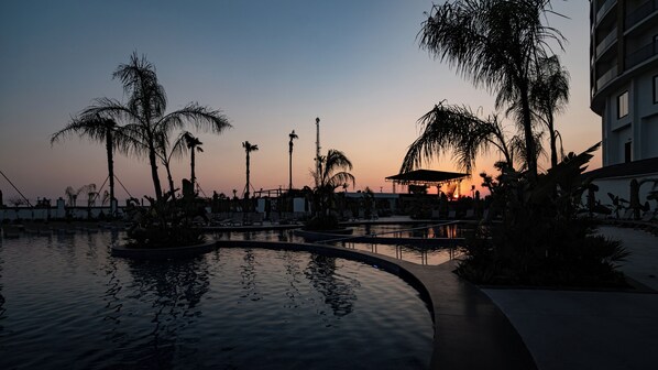 A resort pool area with palm trees and a sunset in the background.