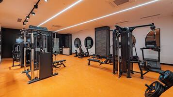 A gym with various exercise equipment, including a squat rack, bench press, and elliptical machines.