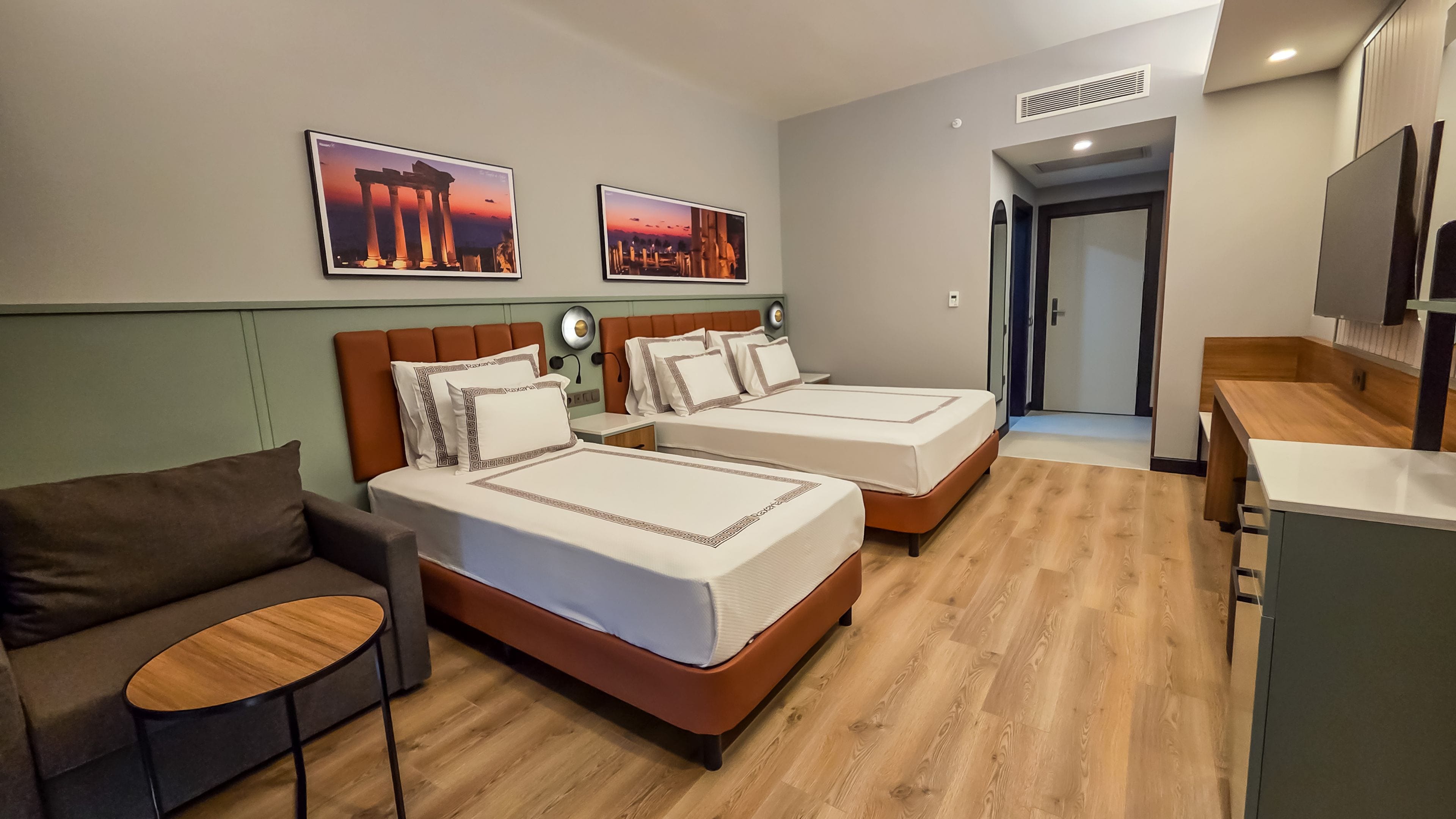 Habitación de hotel con dos camas, un sofá, una mesita y un televisor.
