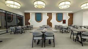 Un salón de conferencias con mesas y sillas, un amplio ventanal y una lámpara moderna.