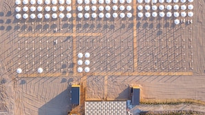 Vista aérea de un amplio espacio al aire libre con varias estructuras hexagonales, posiblemente para eventos o reuniones, junto a una playa y una masa de agua azul clara.