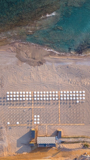 Vista aérea de un amplio espacio al aire libre con varias estructuras hexagonales, posiblemente para eventos o reuniones, junto a una playa y una masa de agua azul clara.
