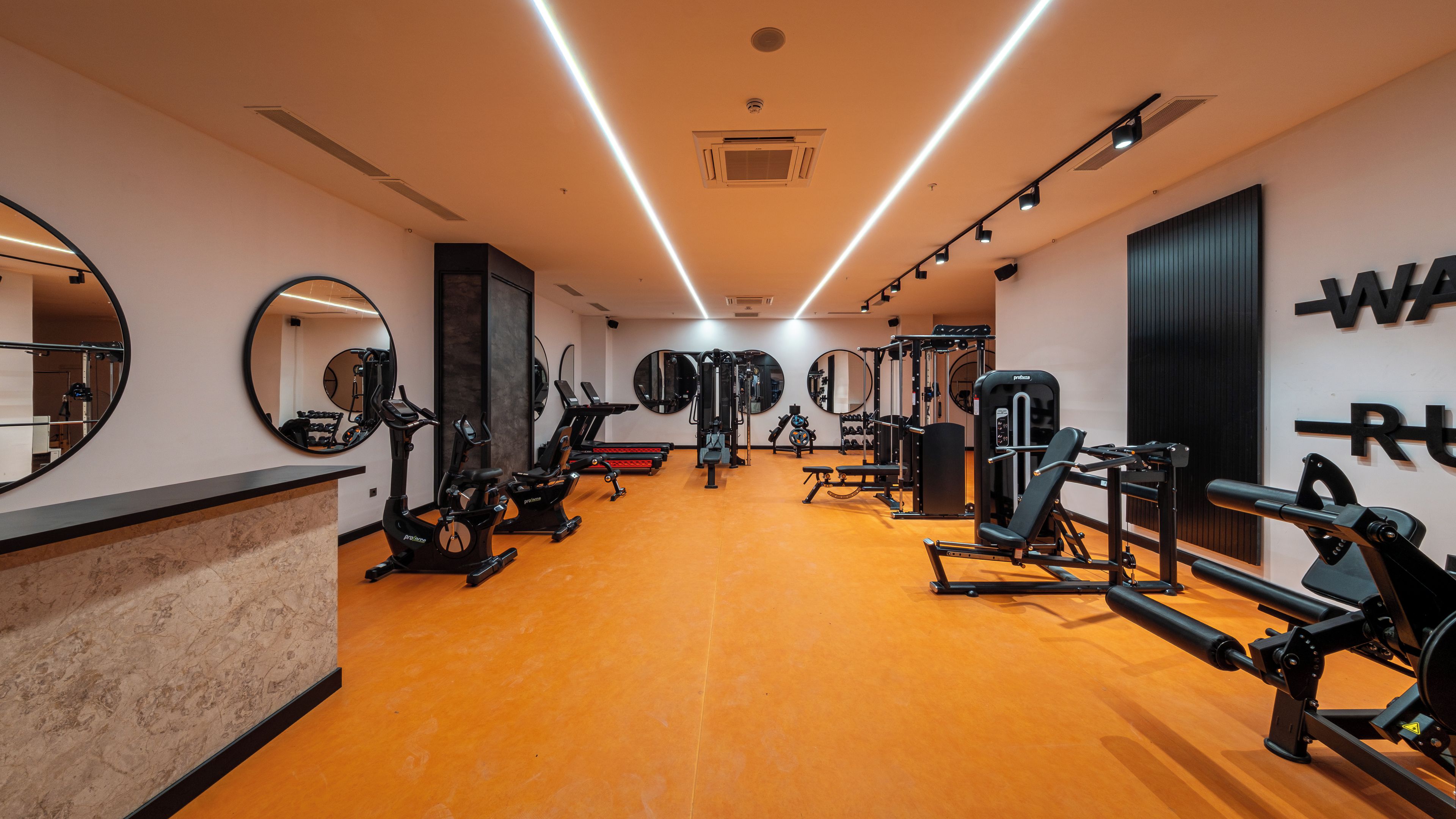 Academia com equipamentos de exercício, espelhos e piso de madeira.