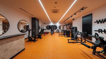 Academia com equipamentos de exercício, espelhos e piso de madeira.