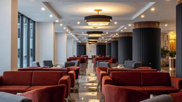 Un vestíbulo de hotel con hileras de sillones tapizados en rojo y gris, piso de mármol e iluminación colgante moderna.
