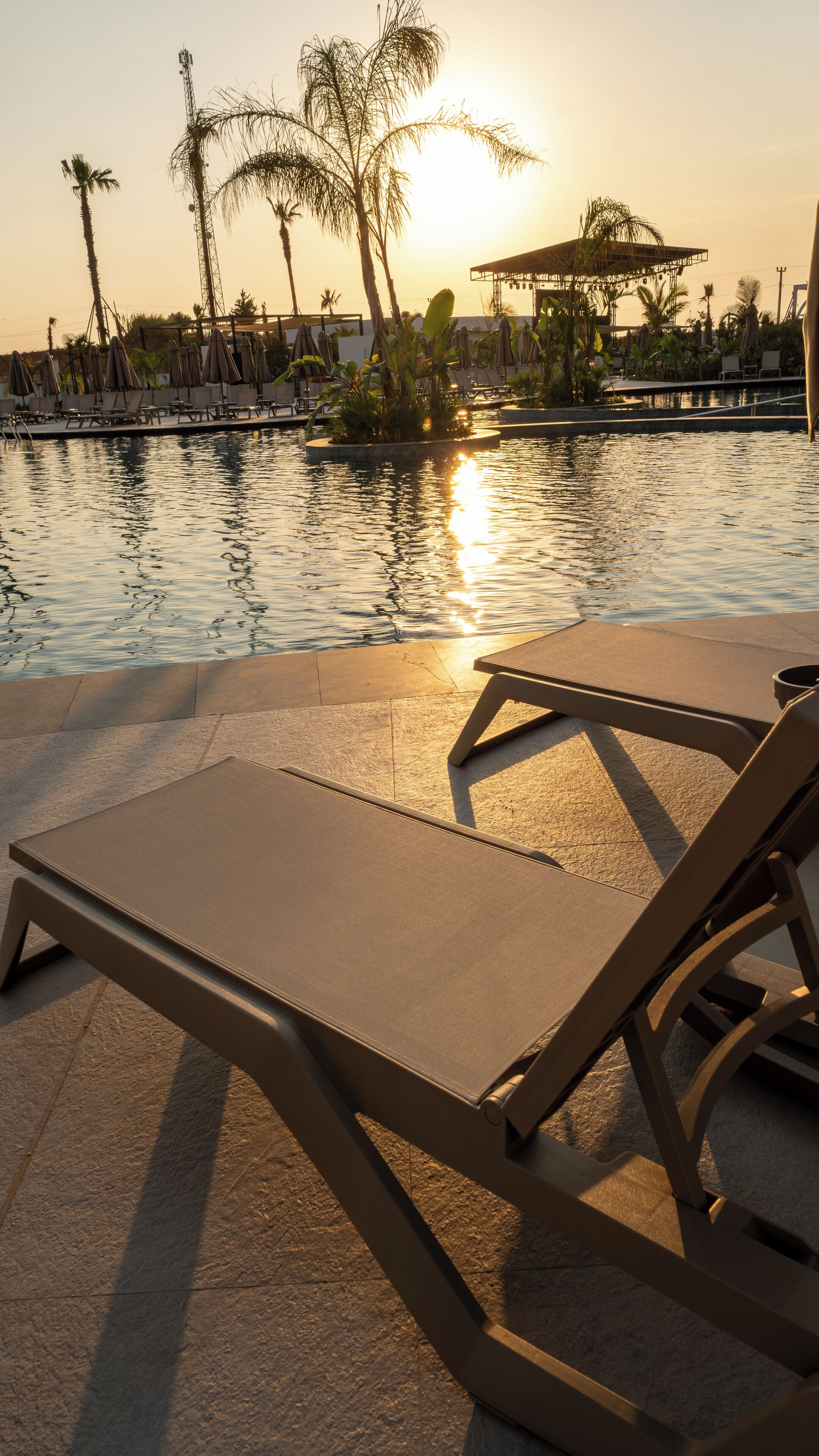 A poolside area with lounge chairs and a view of the sunset over water.