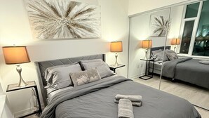 A modern bedroom with a large bed, two bedside tables with lamps, a large mirror, and a decorative wall piece.
