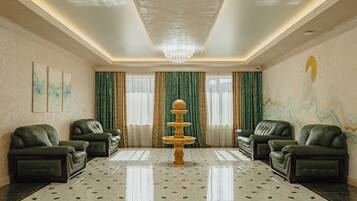 A spacious lobby with a chandelier, green curtains, and a fountain centerpiece.