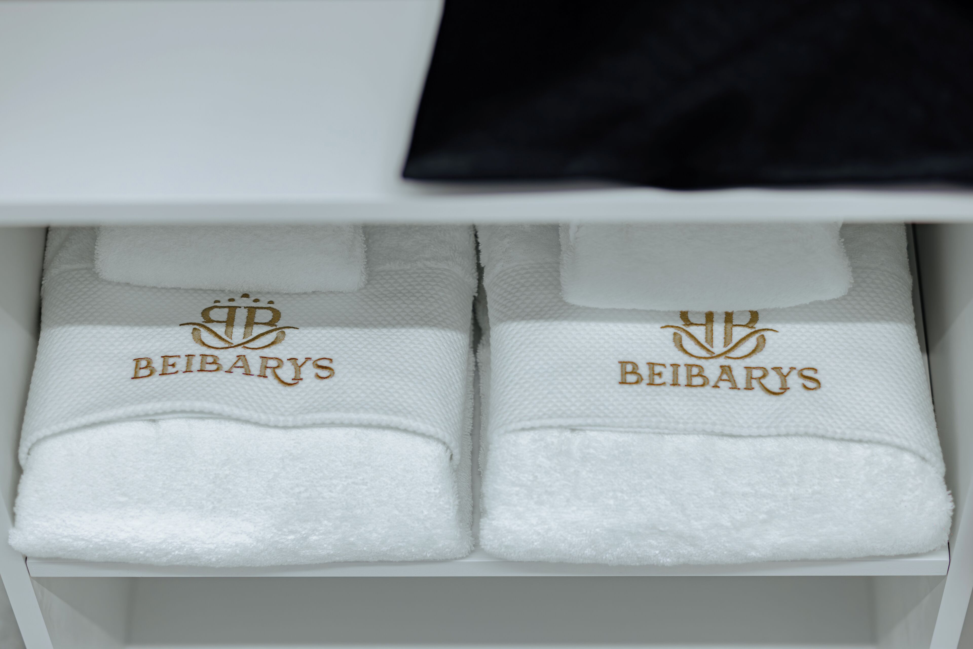 A white shelf with two folded white towels, each with the embroidered text "BEIBARYS".