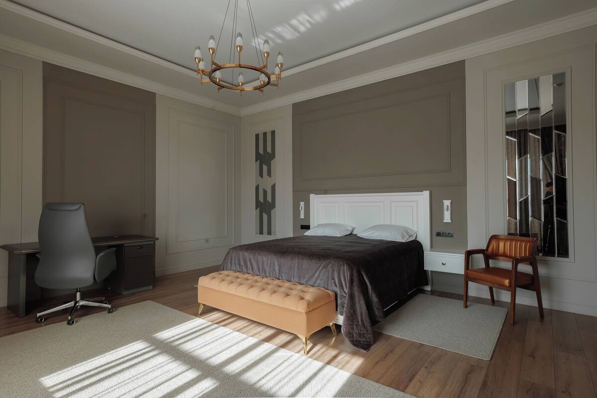 A bedroom with a large bed, a desk, a chair, and a bench.