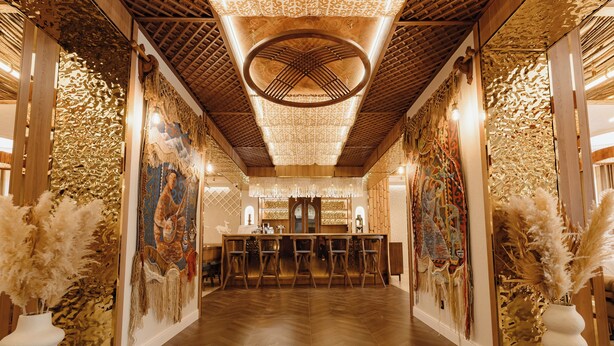 Zona de bar con suelo de madera, taburetes y una barra central.