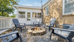 A backyard with a fire pit surrounded by four Adirondack chairs.