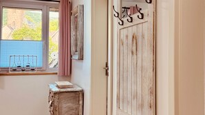A room with wooden flooring, a window with a view of greenery, a rustic door with hooks, and a small table with a balance scale. - Fabian's vacation home / Rurseliebe (Simmerath)