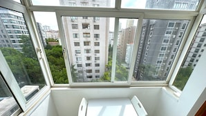 Une pièce d’angle avec une grande fenêtre, une petite table blanche et une vue sur les bâtiments environnants et la verdure.